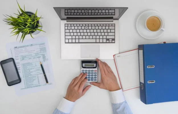 Vue de dessus d'un bureau avec un ordinateur, une calculatrice, des documents fiscaux et un classeur, symbolisant la gestion et le calcul des impôts professionnels.