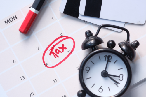 Calendrier marqué du mot "tax" au 14, avec un réveil noir et un marqueur rouge, illustrant une échéance fiscale importante