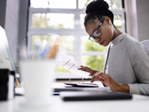 Femme assise à un bureau, vérifiant une facture via une calculette