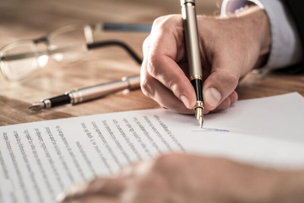 Main d'un homme d'affaire en train de signer avec un stylo un pacte d'actionnaires