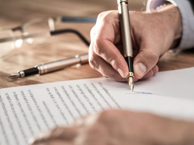 Main d'un homme d'affaire en train de signer avec un stylo un pacte d'actionnaires